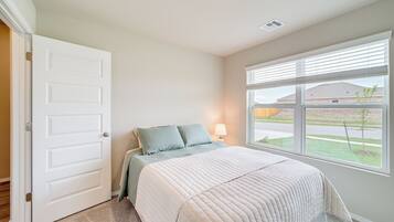 A bedroom with a bed, a window with blinds, a door, and a lamp.