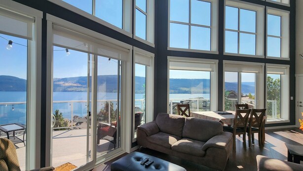 A spacious balcony with a view of the sea and mountains, furnished with a sofa, chairs, and a table. - Bright 3 Bedroom Cottage with Sweeping Lake Okanagan Views! (Kelowna)