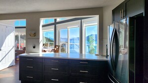 A kitchen with a large window, a refrigerator, and a counter. - Bright 3 Bedroom Cottage with Sweeping Lake Okanagan Views! (Kelowna)