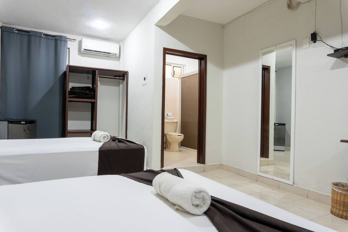 A hotel room with two beds, a bathroom, and a mirror.