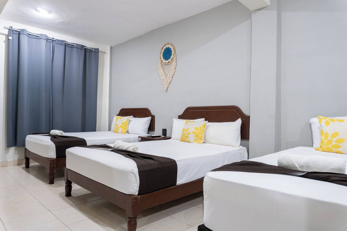 A hotel room with three single beds, a large mirror, a wall decoration, and a curtain.