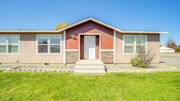 A single-story building with a red and beige exterior, a front door, and a small front yard with a lawn and a few shrubs.