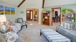 A living room with a sofa, ottoman, armchair, and bookshelf. There is a door leading to a dining area with chairs and a table. - Hike, Golf, Ski & More: Family Home in South Weber (South Weber)