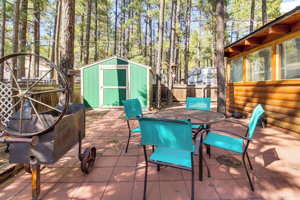 A rustic outdoor patio with a metal cart, green shed, and wooden cabin. - Near Scenic Trails! Woodsy Log Cabin in Lakeside (Lakeside)