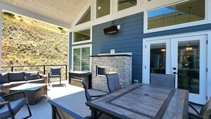 An outdoor patio with a stone fireplace, seating area, and a view of a hillside. - Stunning Modern Cottage at La Casa Lakeside Resort (Kelowna)