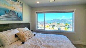 A bedroom with a large bed, a view of a residential area, and a painting on the wall. - Stunning Modern Cottage at La Casa Lakeside Resort (Kelowna)