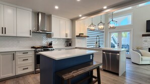 A modern kitchen with white cabinets, a central island, and pendant lighting. - Stunning Modern Cottage at La Casa Lakeside Resort (Kelowna)