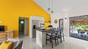 A modern kitchen with a central island, a dining area with chairs, and a TV on a wooden cabinet. - Villa Troupial- Jan Thiel (Jan Thiel)