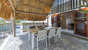 An outdoor dining area with a thatched roof, a wooden table, and white chairs. - Villa Troupial- Jan Thiel (Jan Thiel)