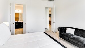 A bedroom with a bed, a black sofa, and a bathroom visible through an open door. - Patio & Pool Access: Family Home in Tomball (Hockley)