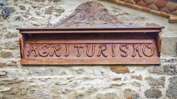 A wooden sign with the word "AGRITURISMO" carved into it, mounted on a stone wall.