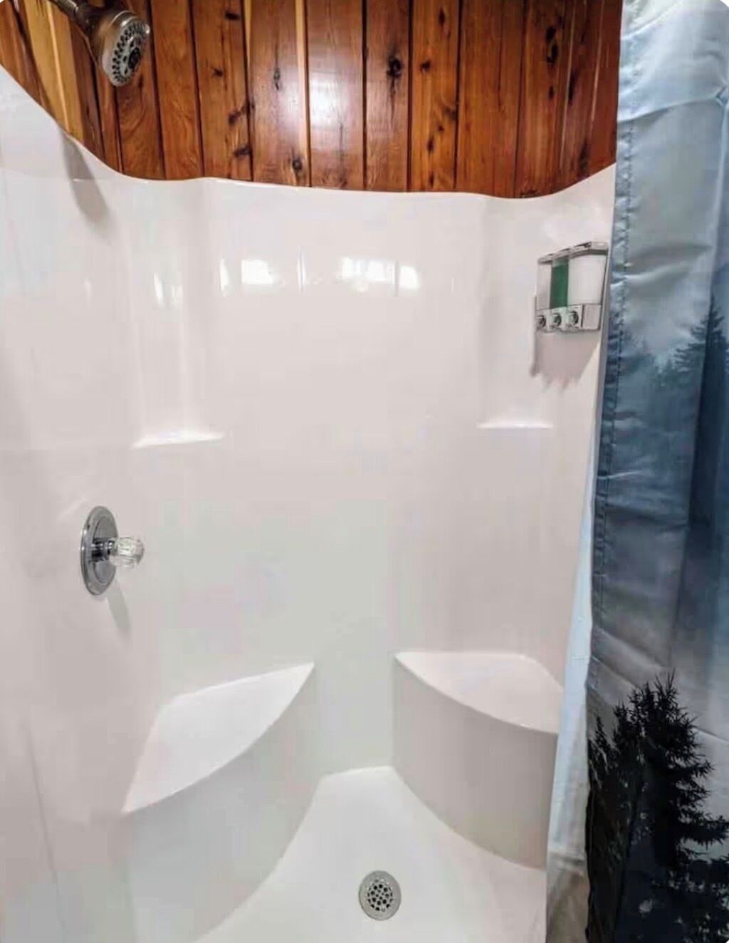Ducha con techo de madera y pared de azulejos blancos.