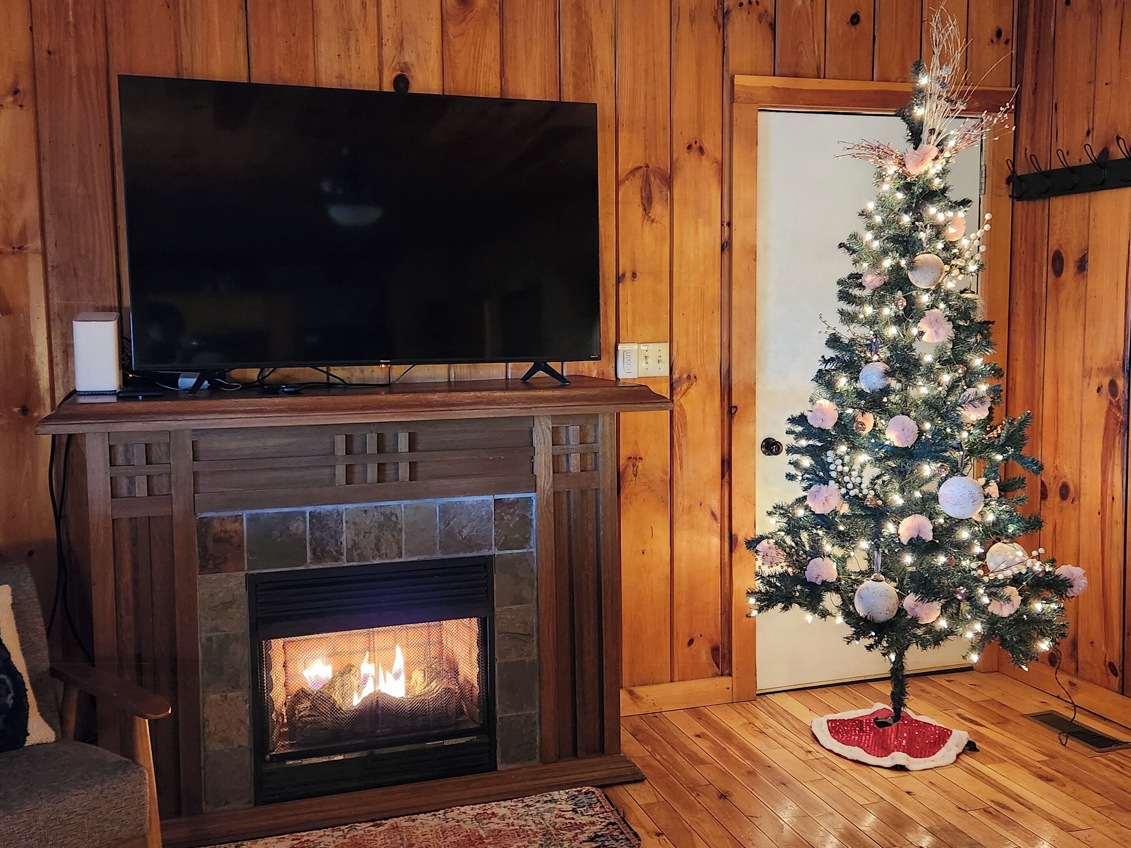 A living room with a fireplace, a television on a stand above the fireplace, and a decorated Christmas tree.