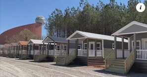 Une rangée de maisons mobiles dotées de porches et d’escaliers à l’avant, se dressant sur un fond de verdure composé d’arbres et d’une grande structure sphérique.
