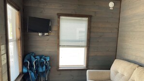 A room with a beige sofa, a television mounted on the wall, and a window with blinds. - Tiny Homes for Rent, minutes to the Casino, Golf Course & Water Park (Philadelphia)