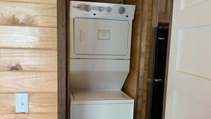 A compact laundry room with a Whirlpool washer and dryer, wooden walls, and a small step leading to the door. - Tiny Homes for Rent, minutes to the Casino, Golf Course & Water Park (Philadelphia)
