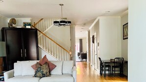 A spacious living room with a light-colored sofa, a glass coffee table, and a dark wooden cabinet. A staircase with a wooden railing leads to another room.