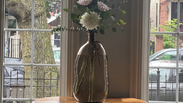 A vase with flowers on a wooden table by a window.