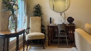 A room with a large window, a round mirror, a chair, a small table, and a sofa.