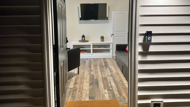 A hallway with a wooden floor, a white console table with decorative items, a television mounted on the wall, and a ceiling fan. - The Cardinal. Newly built 1-bedroom cottage w/ WiFi and AC in delightful Muncie (Muncie)