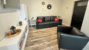 A modern living room with a black leather sofa, a white side table, and a black leather chair. There are decorative plates on the wall and a ceiling fan. - The Cardinal. Newly built 1-bedroom cottage w/ WiFi and AC in delightful Muncie (Muncie)
