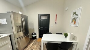 A compact kitchen with a stainless steel refrigerator, a white dining table with two chairs, and a black trash bin. - The Cardinal. Newly built 1-bedroom cottage w/ WiFi and AC in delightful Muncie (Muncie)