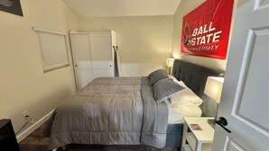 A bedroom with a bed, a nightstand, a lamp, a door, and a red banner on the wall. - The Cardinal. Newly built 1-bedroom cottage w/ WiFi and AC in delightful Muncie (Muncie)
