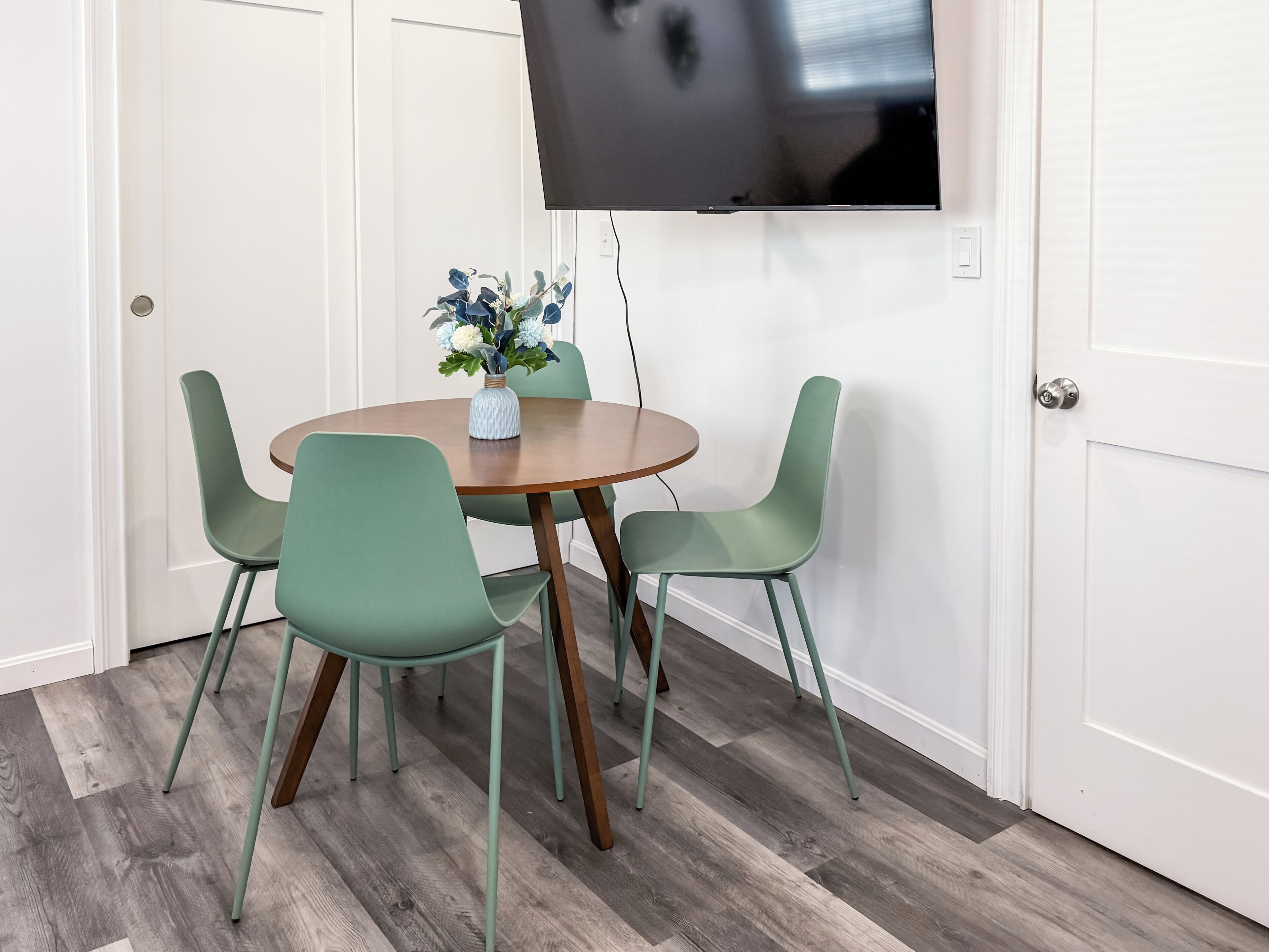 Un coin repas avec une table ronde, quatre chaises vertes et un vase rempli de fleurs.