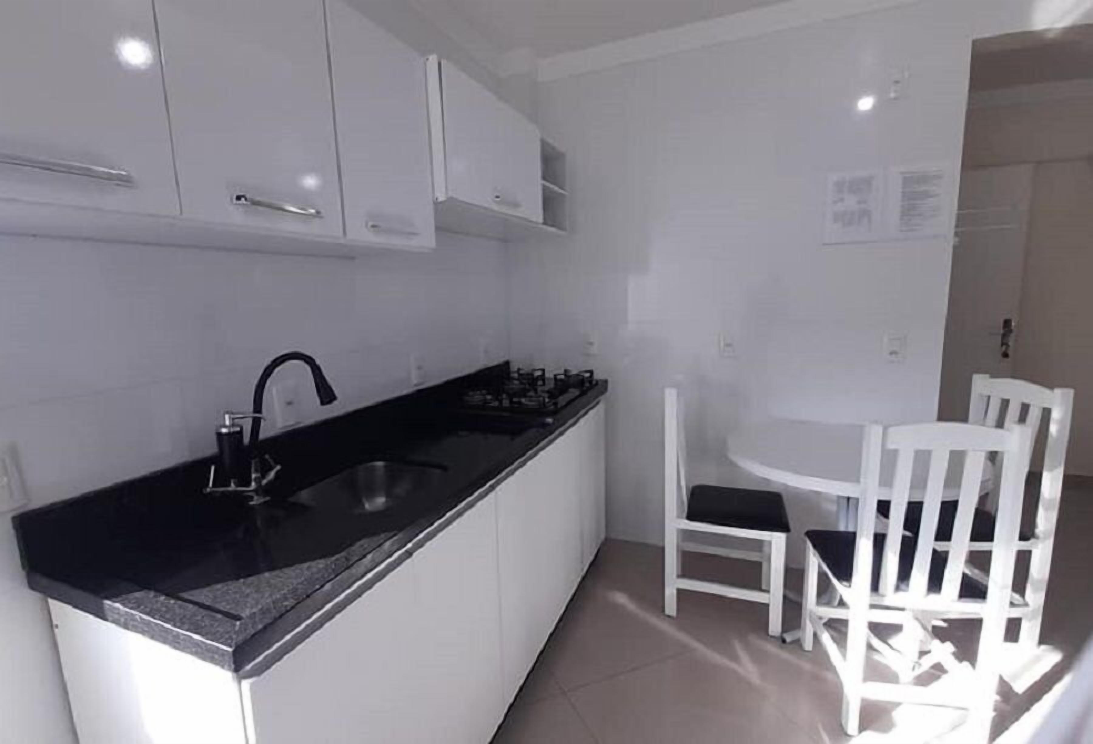 Une cuisine compacte avec des meubles blancs, un plan de travail noir et un petit coin repas avec des chaises blanches.