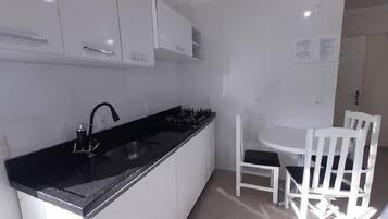 Une cuisine compacte avec des meubles blancs, un plan de travail noir et un petit coin repas avec des chaises blanches.