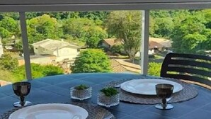 Een tafel voor twee, gedekt met borden, bestek en glazen, op een balkon met uitzicht op een groen landschap.