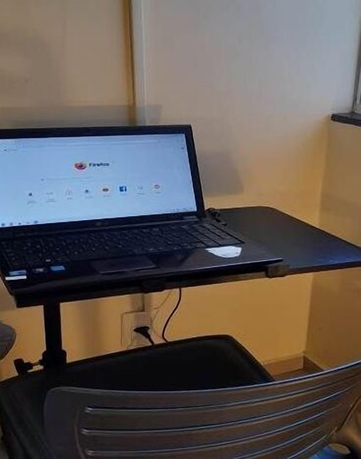 Um laptop sobre uma pequena mesa num quarto com janela.