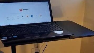 Um laptop sobre uma pequena mesa num quarto com janela.