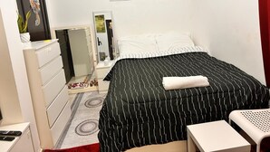 Ein Schlafzimmer mit einem schwarz-weiß gestreiften Bettbezug, einem weißen Kommoden und einem Spiegel, sowie einem Bild an der Wand.