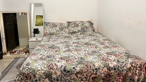 Ein Schlafzimmer mit blumigem Bettbezug, einem Spiegel und einem Wandbild.