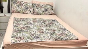 Ein Bett mit blumigem Bettbezug und passenden Kissen, ein weißer Nachttisch und ein roher, sechseckiger Boden.