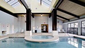 Una amplia piscina interior con un centro circular, rodeada de sillas de descanso y una zona cubierta con tragaluces.