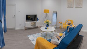 Un salon moderne avec un canapé, un téléviseur, une lampe et des œuvres d’art accrochées au mur.
