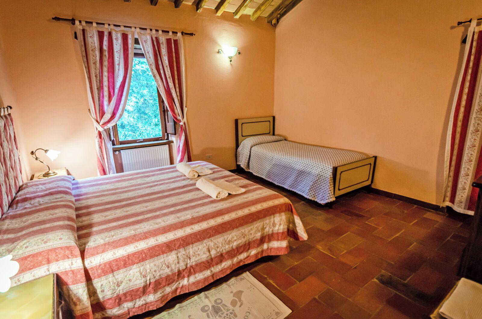 Un dormitorio con dos camas, una ventana con cortinas, una lámpara de pared y un radiador.