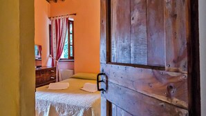 Una habitación rústica con una puerta de madera, una cama con cubrecama blanco y una ventana con cortinas rojas.