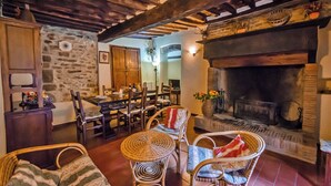 Un interior rústico con pared de piedra, una mesa de comedor de madera, sillas de mimbre y una chimenea.
