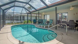 Ein Poolbereich mit Glasveranda, Liegestühlen und einer Essbereich mit Tischen und Stühlen.