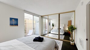 Ein Hotelzimmer mit einem großen Bett, einer Glastür, die auf einen Balkon führt, einem großen Spiegel und einem kleinen Nachttisch.