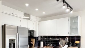 Eine moderne Küche mit weißen Schränken, einem Edelstahlkühlschrank, einer schwarzen Küchenzeile und einem schwarz-weißen Schachbrettfußboden.
