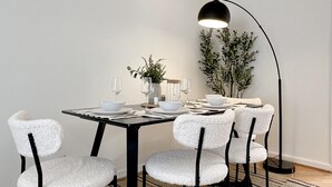 Ein Essbereich mit einem quadratischen Tisch, sechs weißen Stühlen, schwarzen Metallbeinen und einer schwarzen Stehlampe.