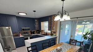 Een moderne keuken met donkerblauwe kastjes, roestvrijstalen apparatuur en een houten eettafel met stoelen.