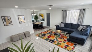 Een moderne woonkamer met een bank, een bijzettafeltje en een eethoek op de achtergrond.