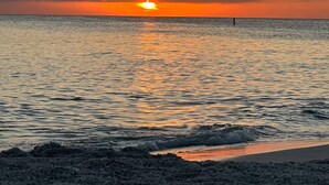 Een zonsondergang boven een strand met rustig water en een rotsachtige kustlijn.