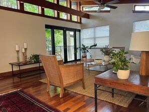 Relax in a spacious living area with a high ceiling and exposed beams, featuring a dining table and balcony with lush greenery views.