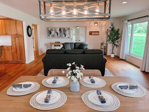 Una sala de estar moderna con un sofá gris oscuro, suelo de madera y un comedor con platos blancos y servilletas azules.
